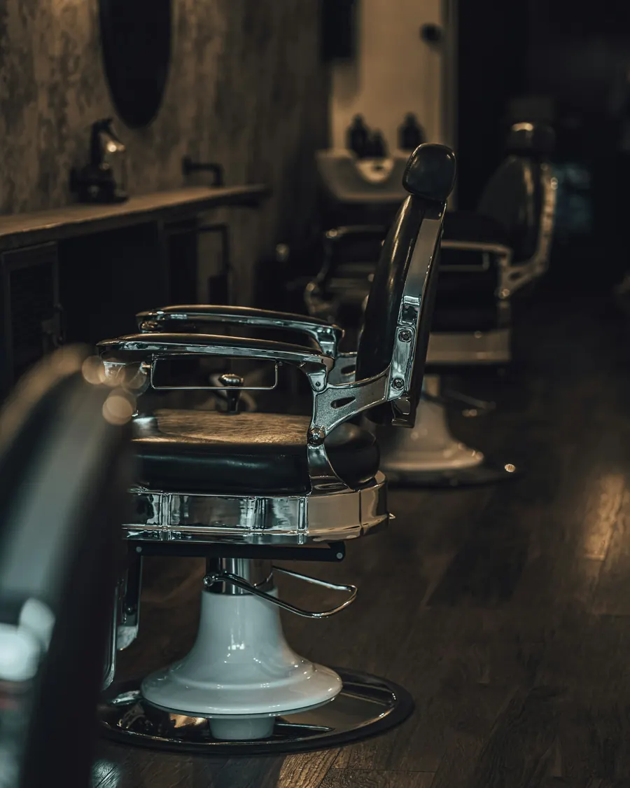 A chrome and black leather barber chair on a dark wood floor