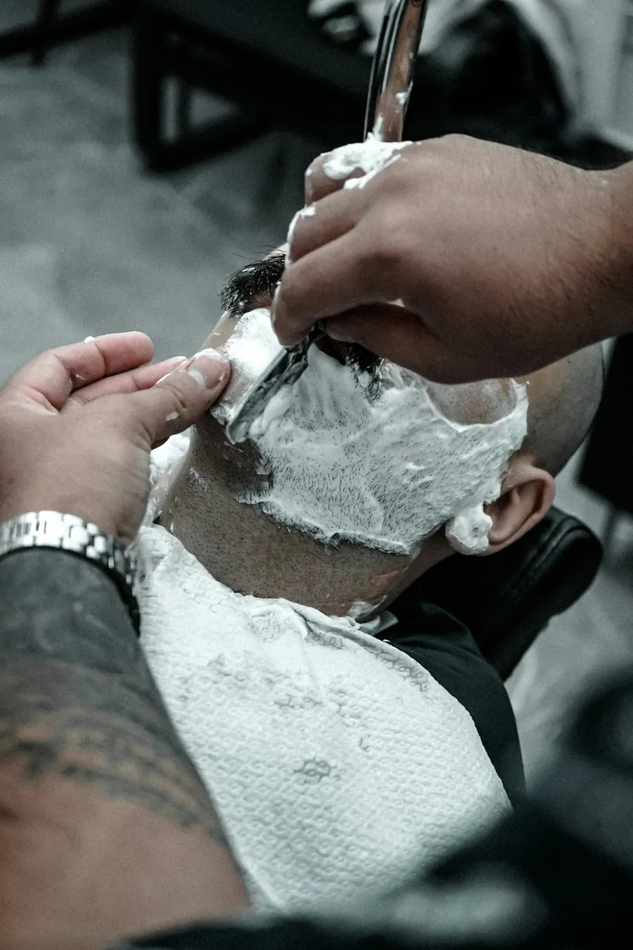A barber shaving a lathered jawline with a straight razor