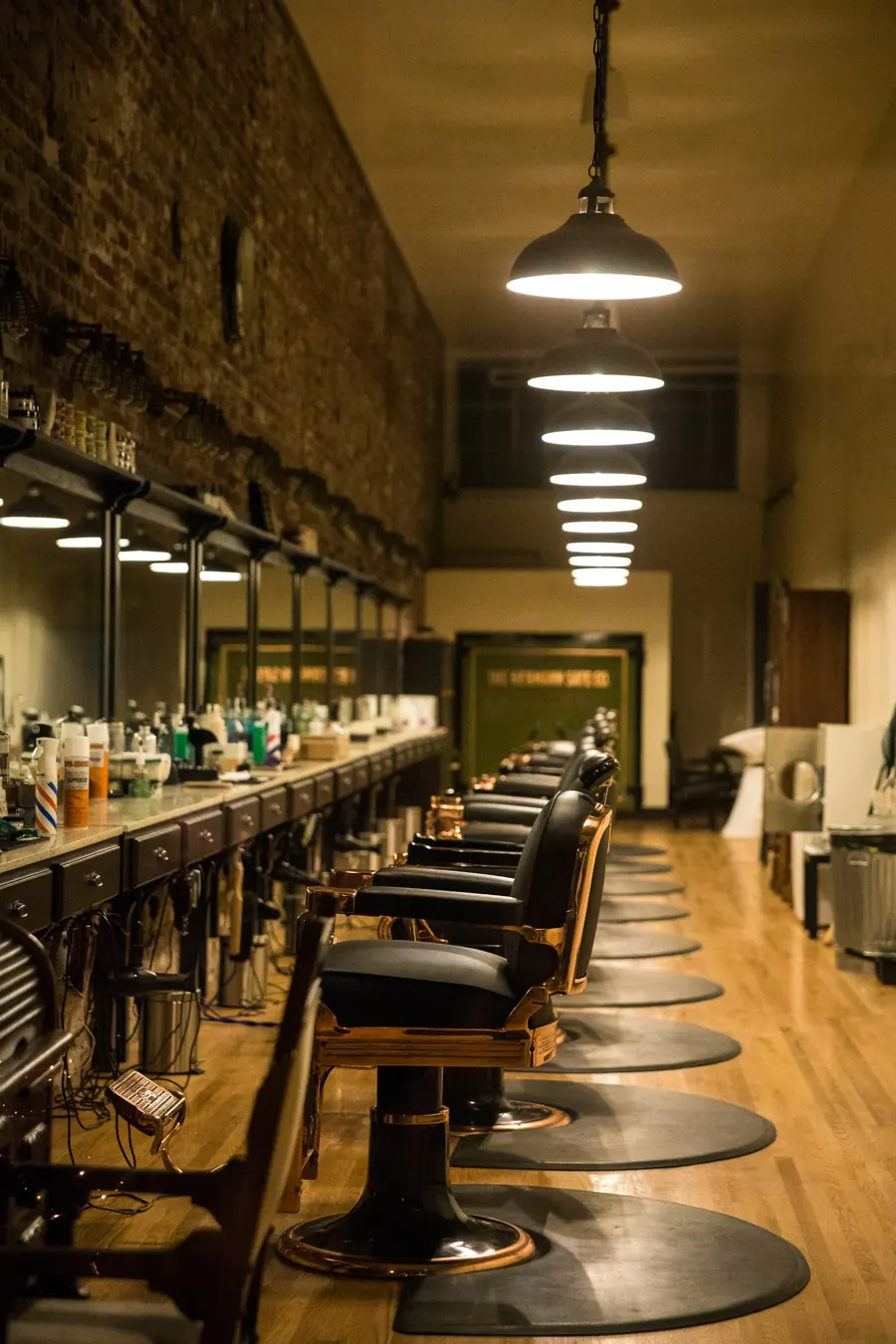A long row of barber chairs and mirrors down a narrow shop under hanging lamps