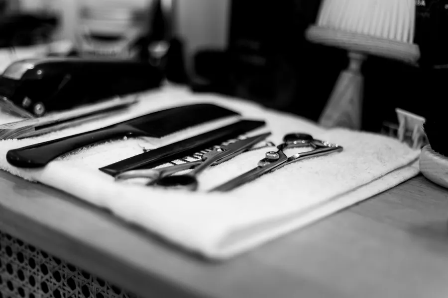 Black and white photo of combs, shears and razors laid out on a white towel at a barber station